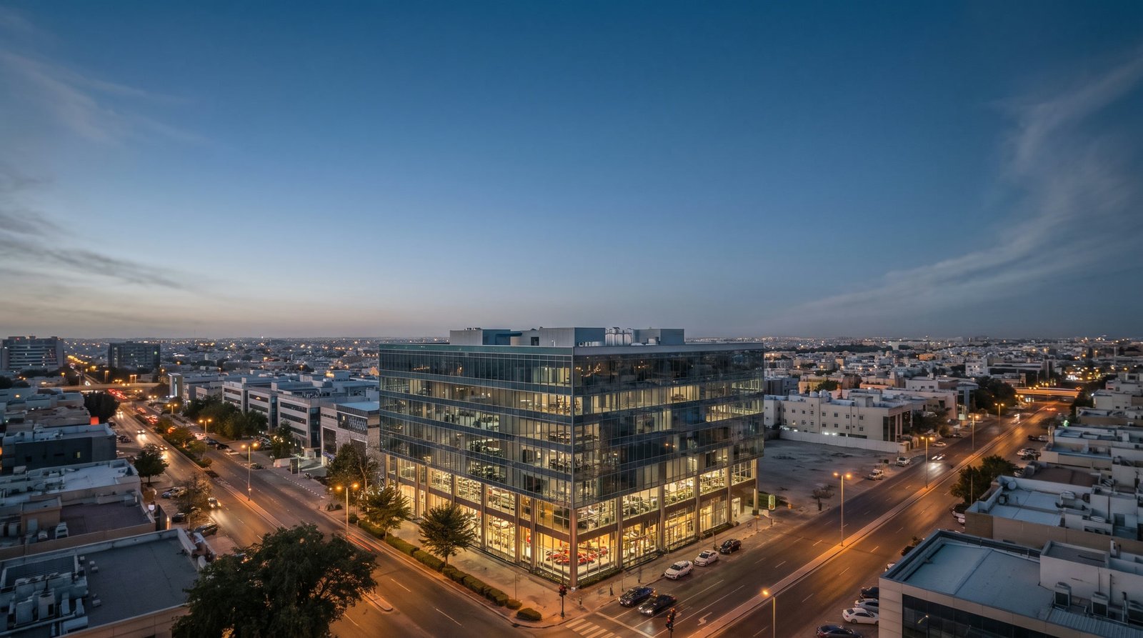 CBC Tower at blue hour seen from the air, its glass glowing gold over the boulevards of Erbil